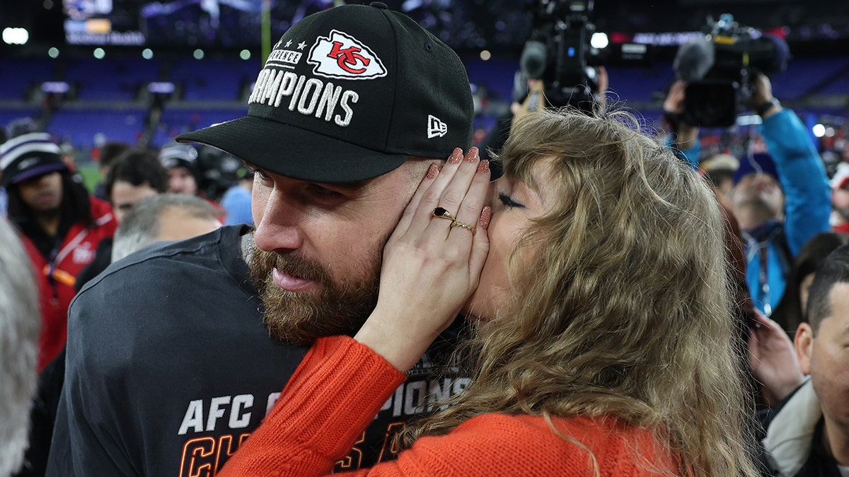 Taylor Swift con un jersey rojo susurra al oído de Travis Kelce en el campo de fútbol americano después de que los Kansas City Chiefs ganaran el Campeonato de la AFC.