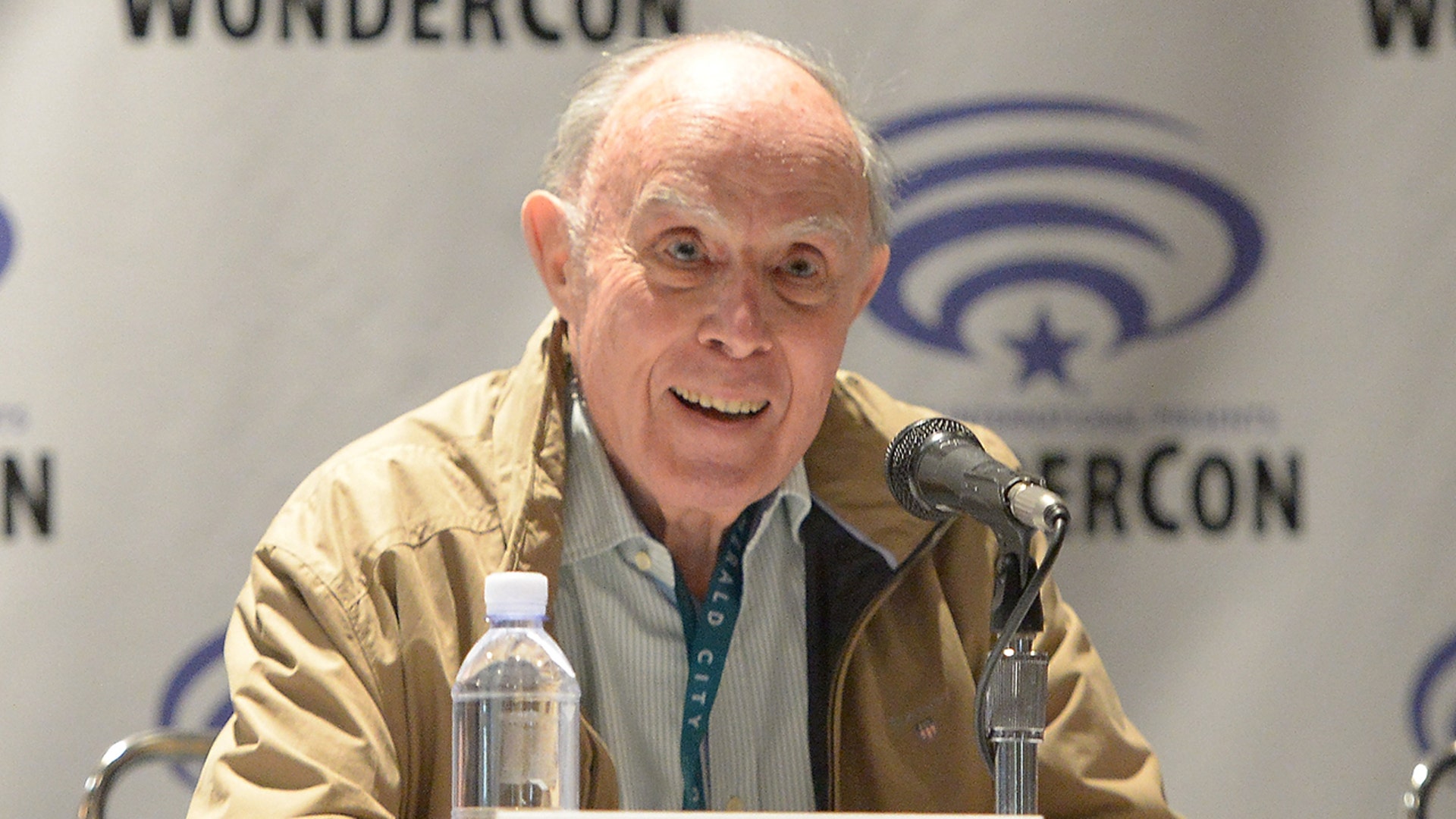 David Graham sitting during a panel wearing a tan jacket