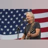 Kris Kristofferson singing and playing guitar in front of American flag