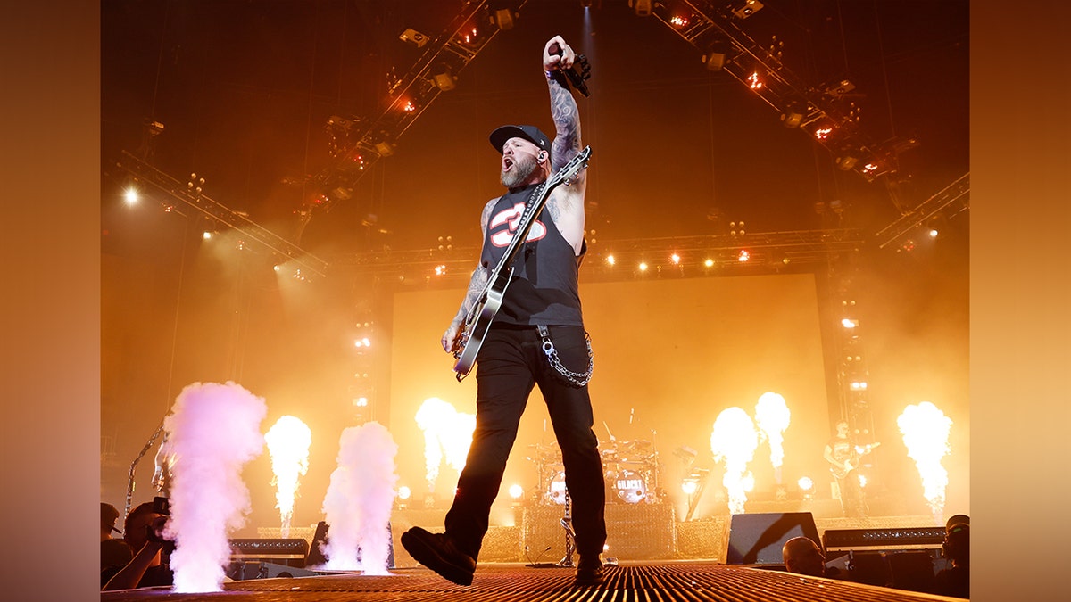 Brantley Gilbert pumps his fist in the air, dressed all in black, as fire flashes on stage behind him