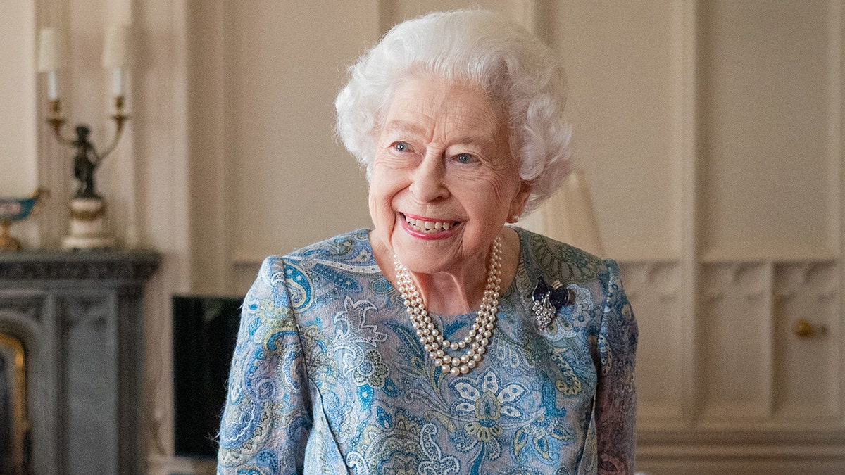 Queen Elizabeth smiles and looks into the distance in a patterned blue dress and pearl necklaces at Windsor Castle