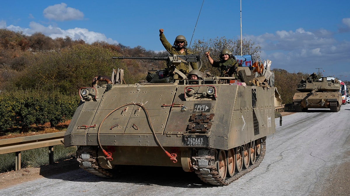 Israeli soldiers raise their fists from a moving APC in northern Israel near the Israel-Lebanon border