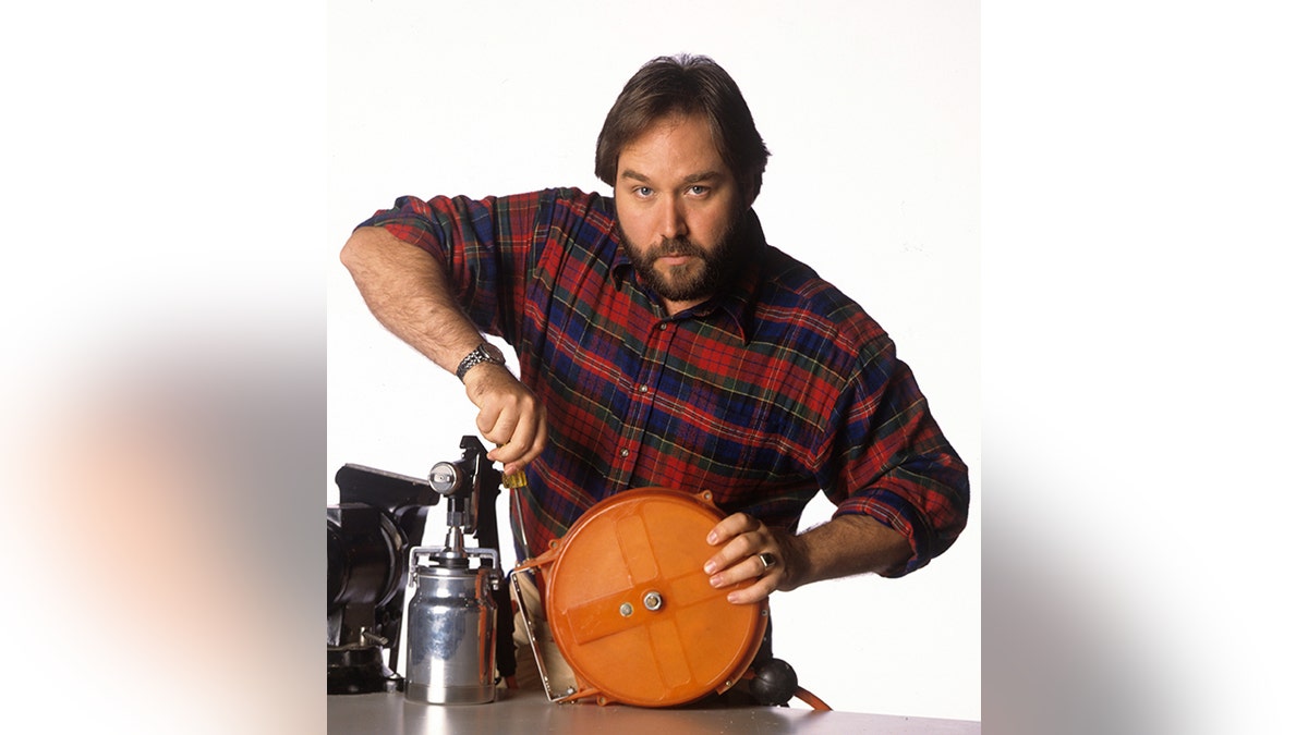 Richard Karn in a red plaid shirt holds some type of machinery in character for "Home Improvement"