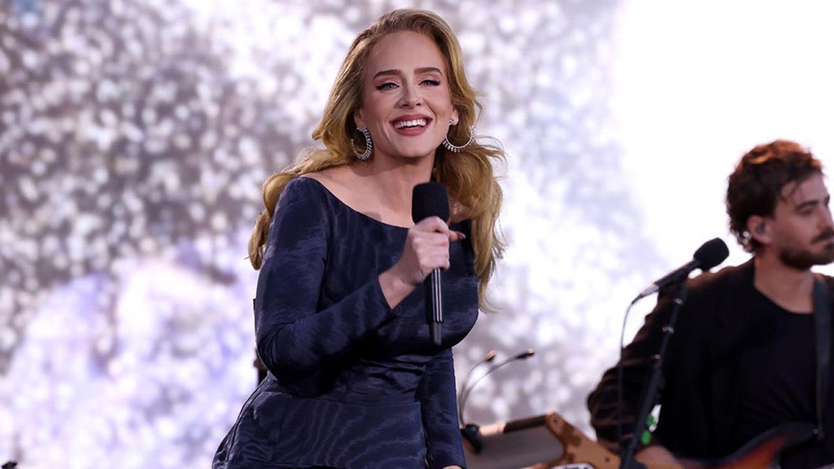 Adele in a blue dress smiles as she performs in Munich