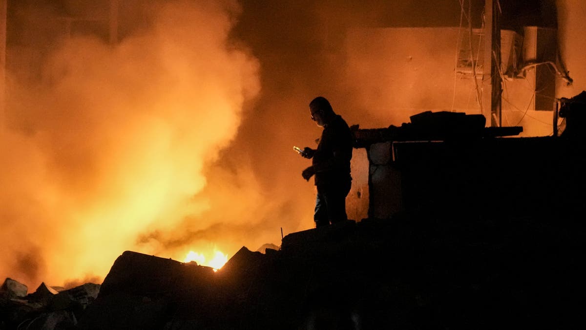 Un hombre usa su teléfono móvil mientras las llamas y el humo se elevan en la escena de los edificios afectados por un ataque aéreo israelí en el centro de Beirut, Líbano, el jueves 10 de octubre de 2024. (Foto AP/Bilal Hussein)