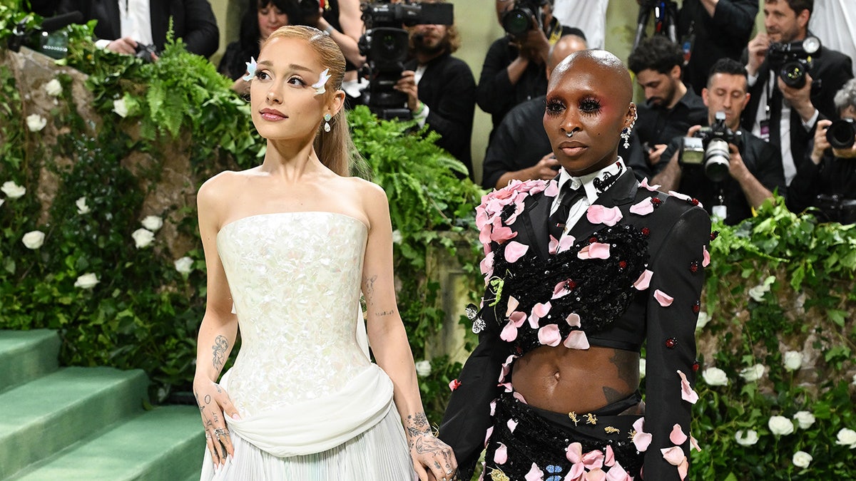 Ariana Grande and Cynthia Erivo holding hands connected  the Met Gala stairs