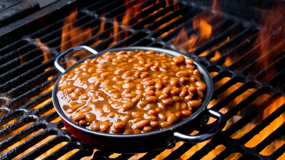 Barbecue baked beans are shown connected  a flaming grill.