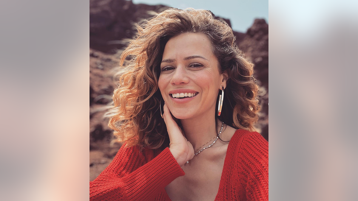 Bethany Joy Lenz dans un pull rouge met sa main sur son cou