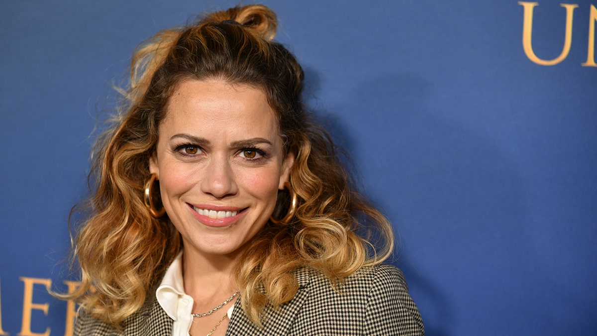 Bethany Joy Lenz in een geruite blazer en ombré haar glimlacht op het tapijt