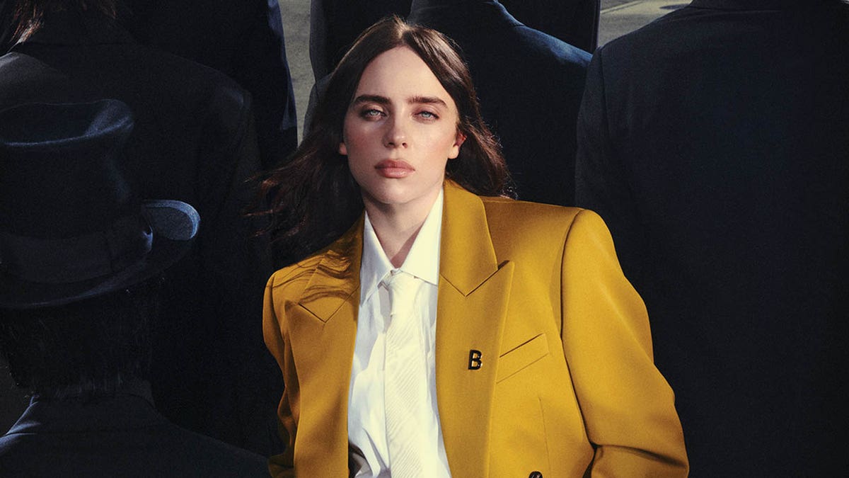 billie eilish successful  a yellowish  suit   with shadows of men with apical  hats successful  the background