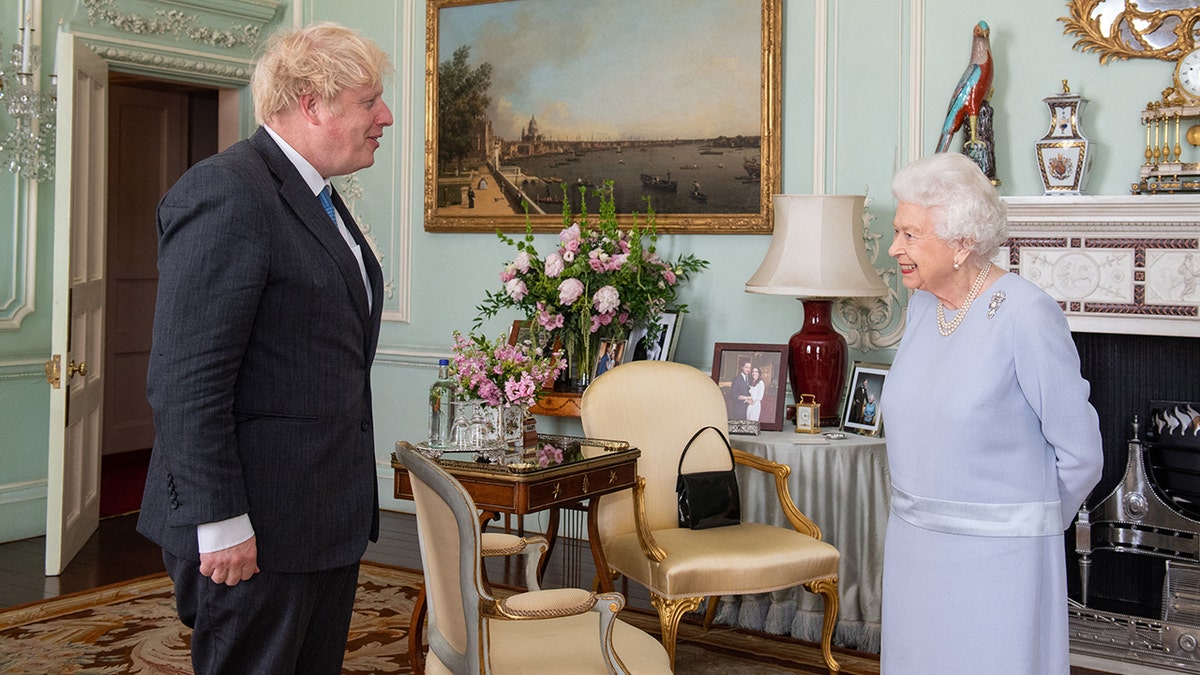 Boris Johnson in a black suit greets Queen Elizabeth in a very pale blue dress at Buckingham Palace