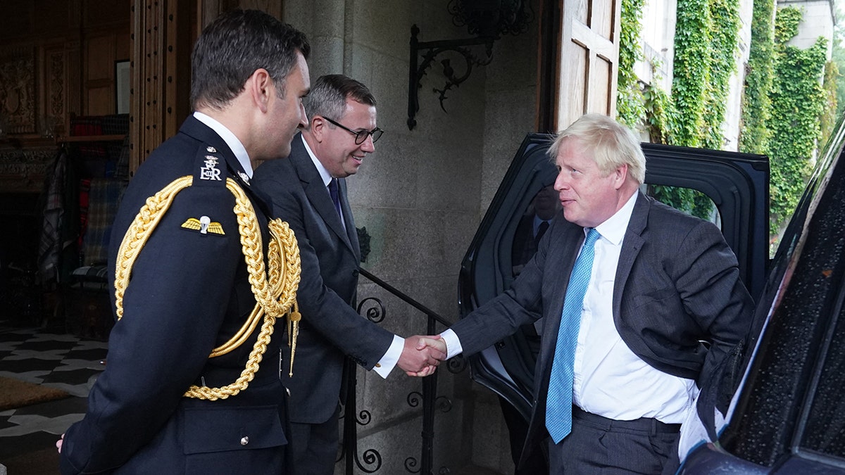 Boris Johnson con traje y corbata azul brillante estrecha la mano del Teniente Coronel de Caballería Tom White y de su Secretario privado Sir Edward Young antes de su visita a la Reina