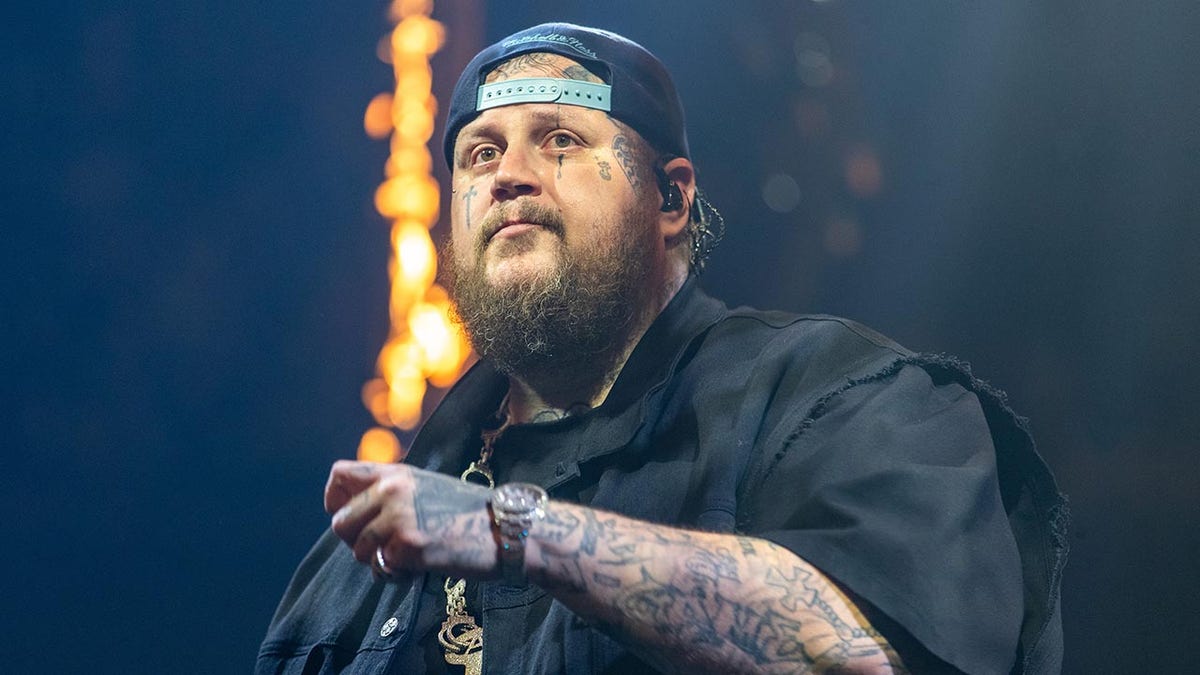 Jelly Roll in a black shirt and backwards hat looks into the distance during a performance