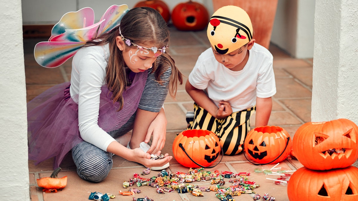 Una niña y un niño disfrazados inspeccionan sus caramelos de Halloween .