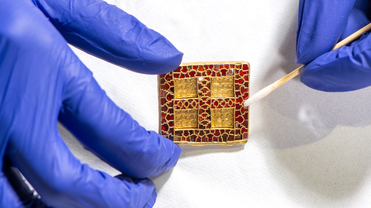 A person cleaning an ancient pendant