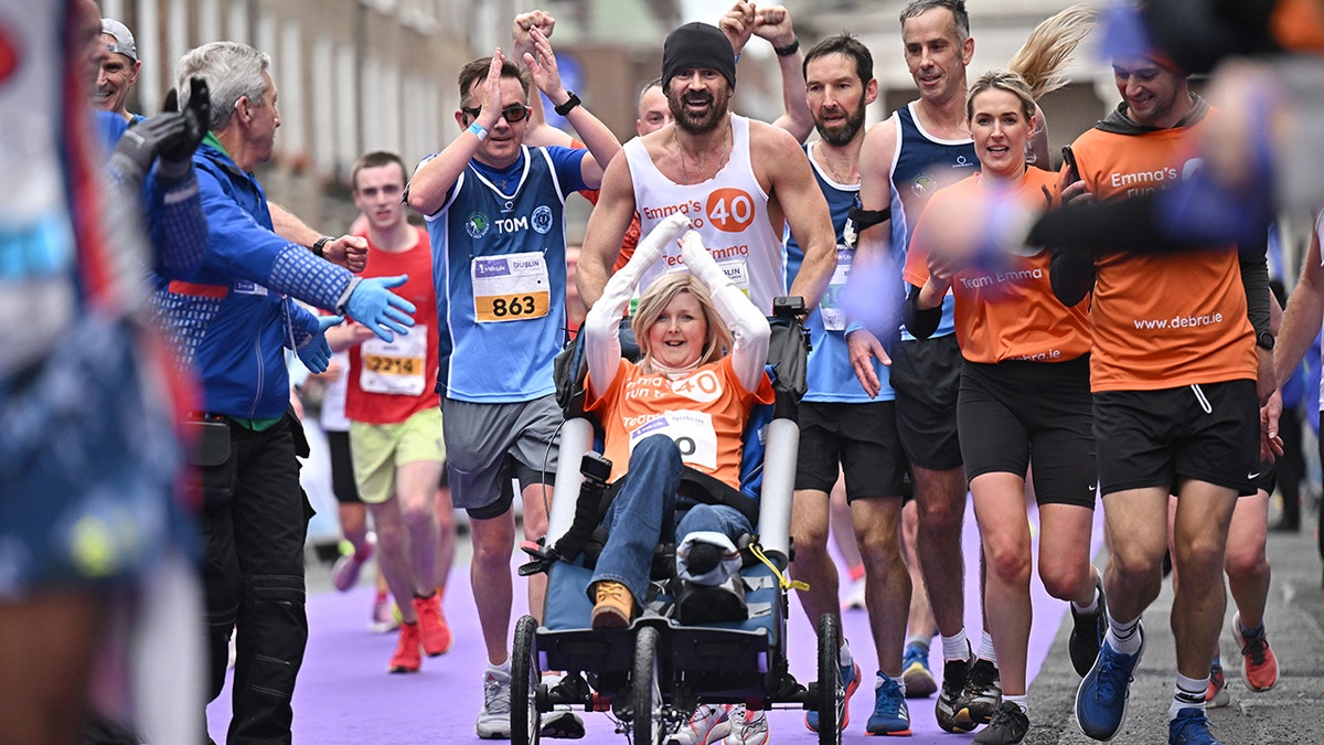 Colin Farrell empuja a Emma Fogarty en silla de ruedas a través de la línea de meta del maratón de Dublín.