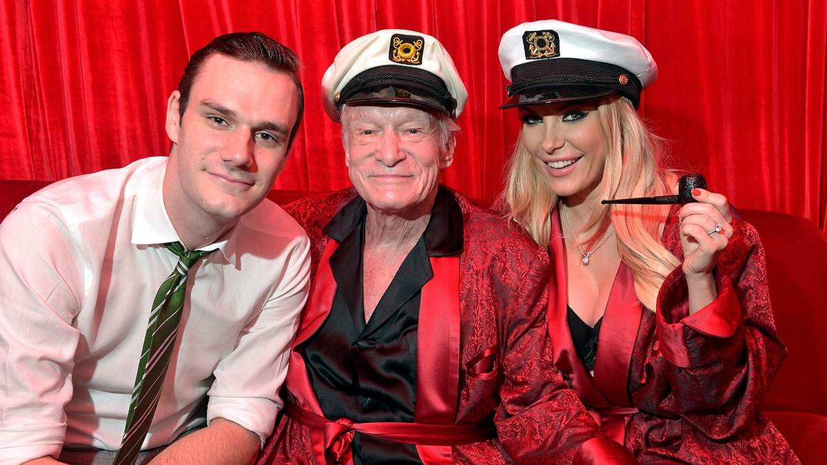 Cooper Hefner, successful  a achromatic  garment  smiles with begetter  Hugh Hefner successful  a reddish  rob and sailors chapeau  adjacent  to woman  Crystal Hefner successful  a akin  outfit 