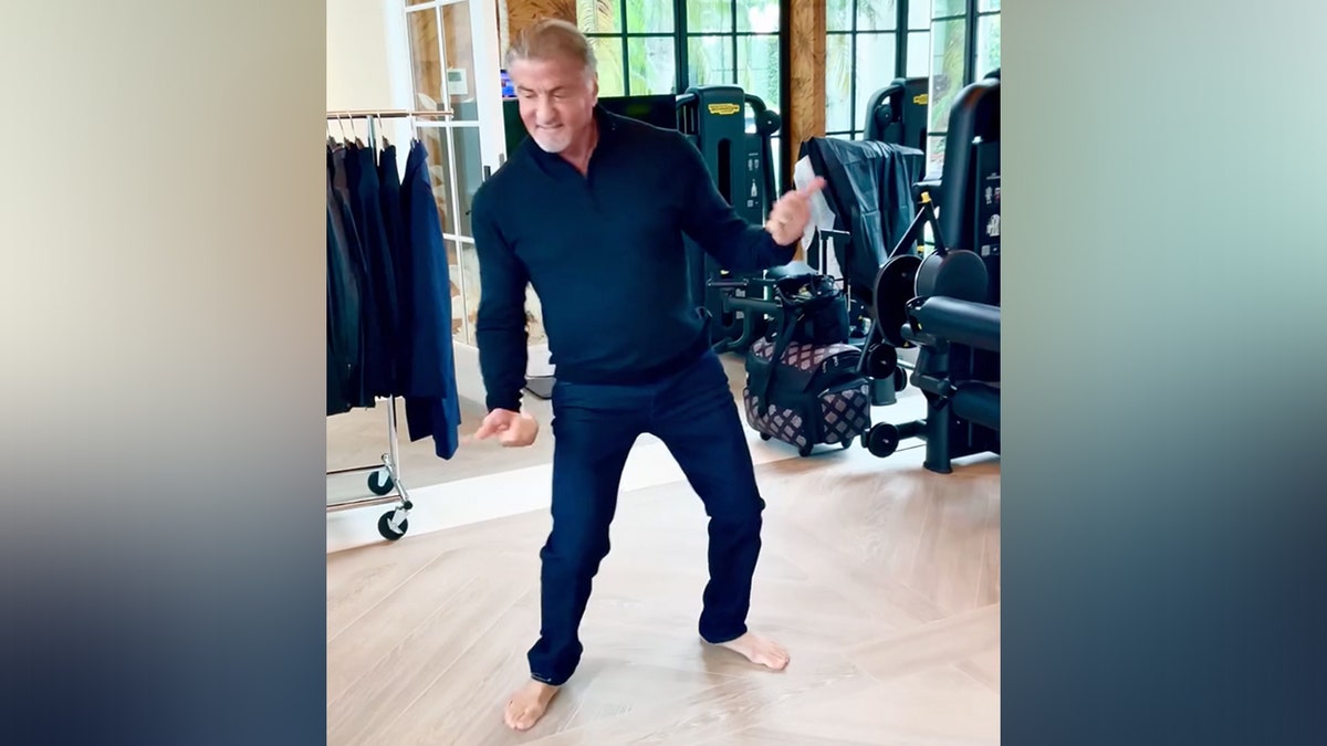 Sylvester Stallone in blue pants and shirt leans to the side as he dances