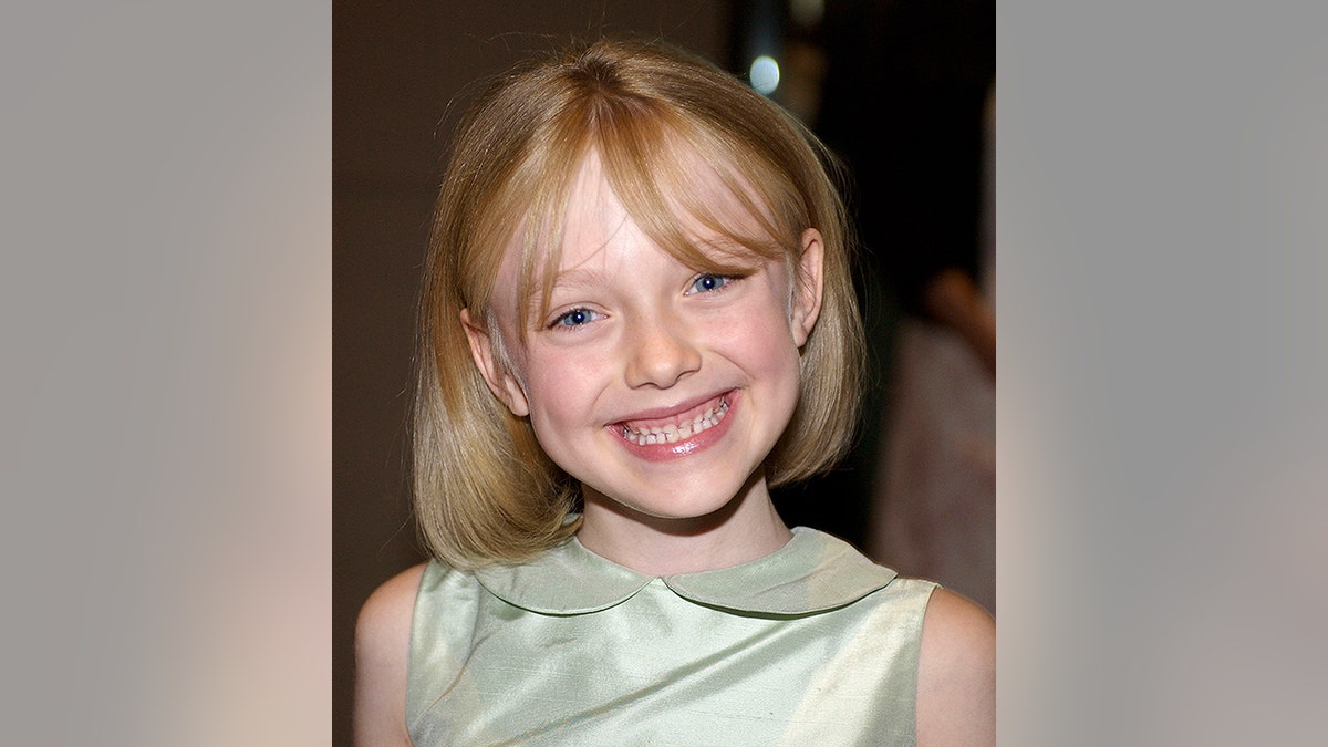 A young Dakota Fanning smiles and bows her head in a bright green dress