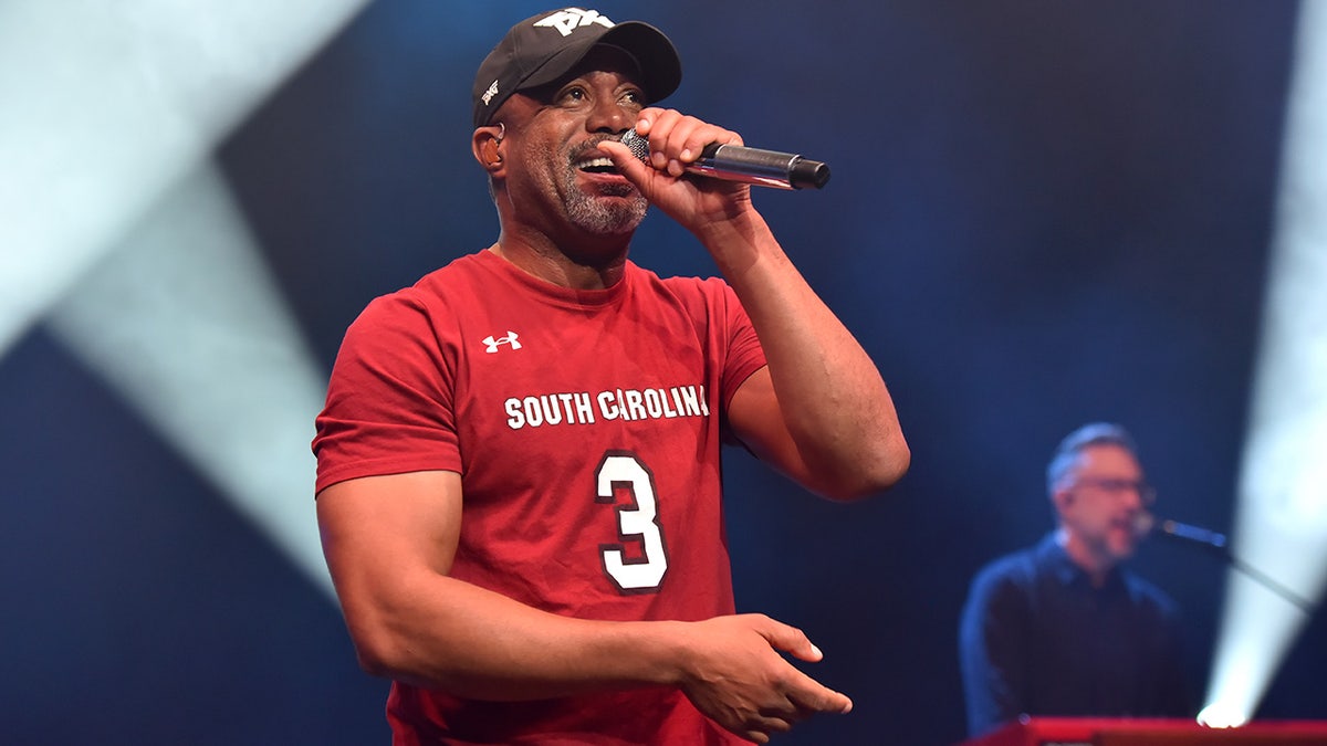 Darius Rucker singing on stage in a red shirt.