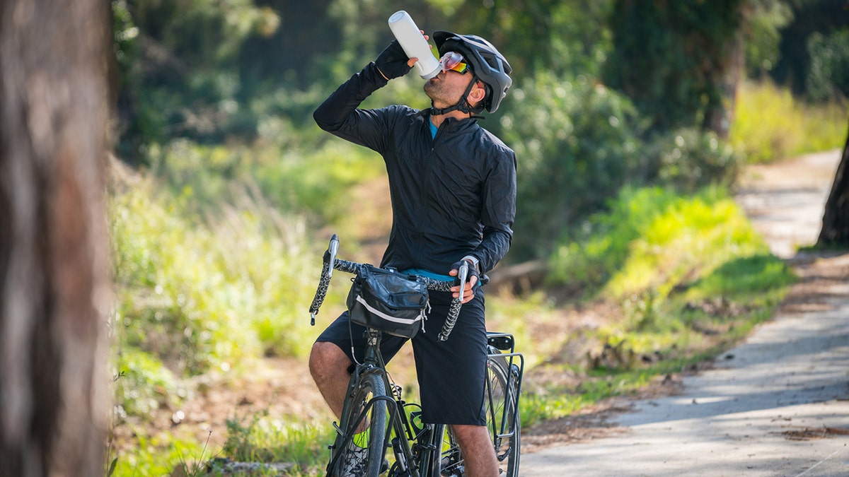 man stopping on bicycle to drink water