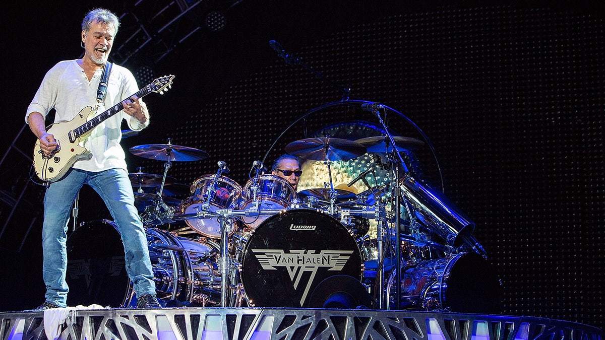 Eddie Van Halen playing guitar on stage with Alex Van Halen on drums behind him