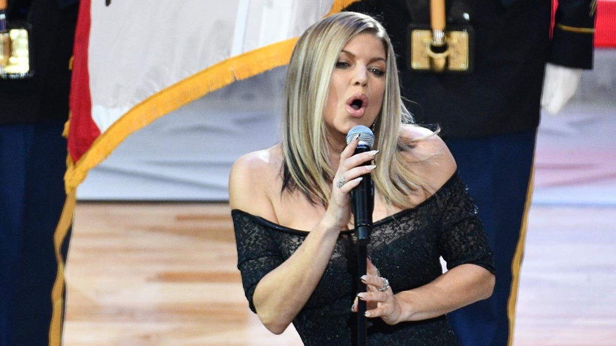 Fergie In sings animatedly into the microphone at the NBA All-Star Game in a black off-the-shoulder dress