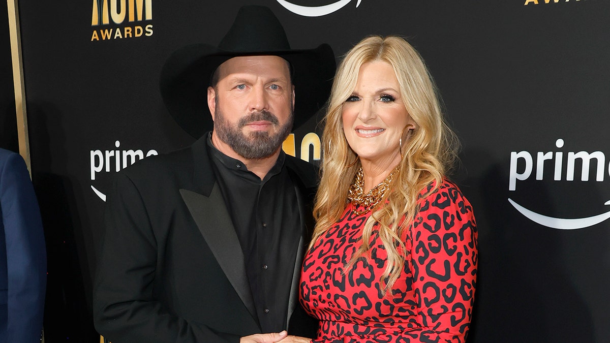 Garth Brooks successful  a achromatic  suit   and cowboy chapeau  poses with woman  Trisha Yearword successful  a reddish  cheetah people     formal  connected  the carpet