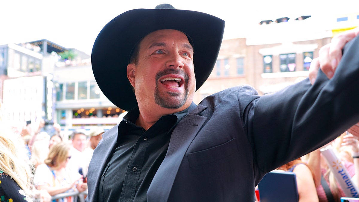 Garth Brooks parece extasiado mientras saluda a sus fans con un sombrero y un traje negros