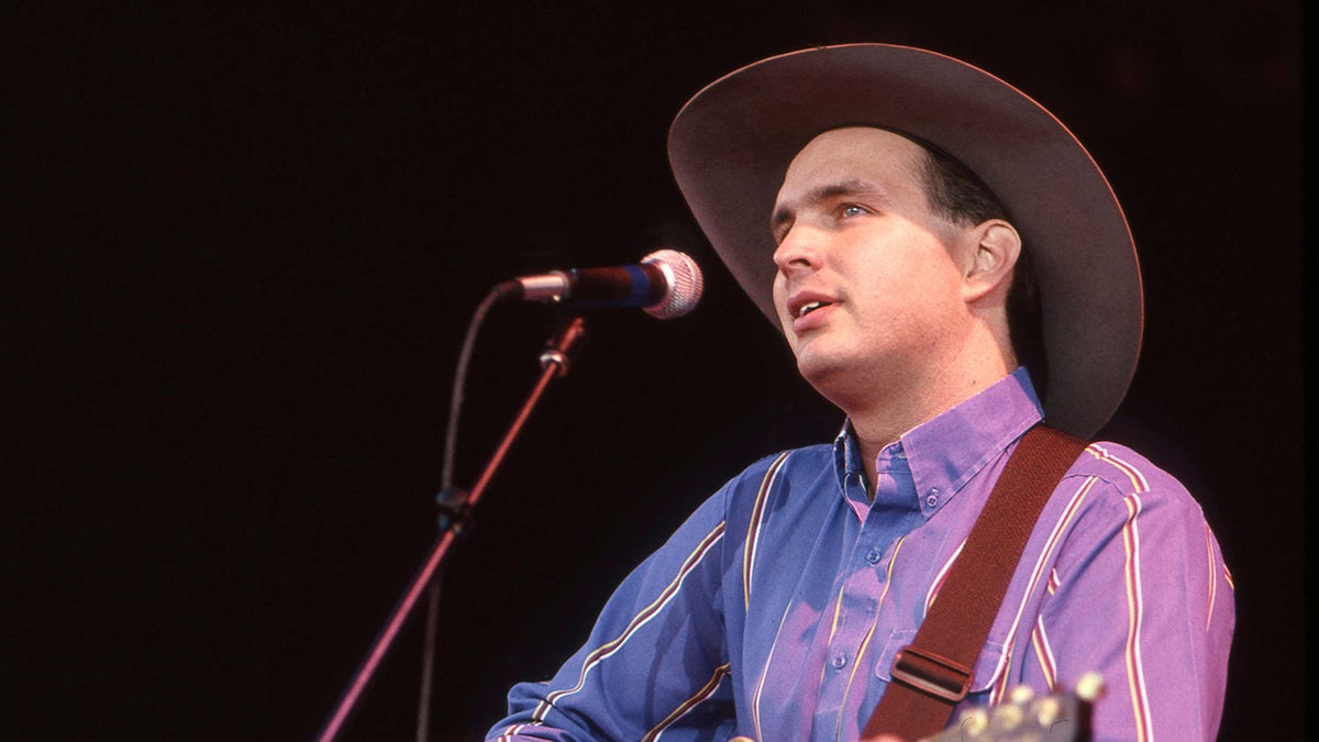 A youger Garth Brooks wears a cowboy chapeau  and sings into a microphone