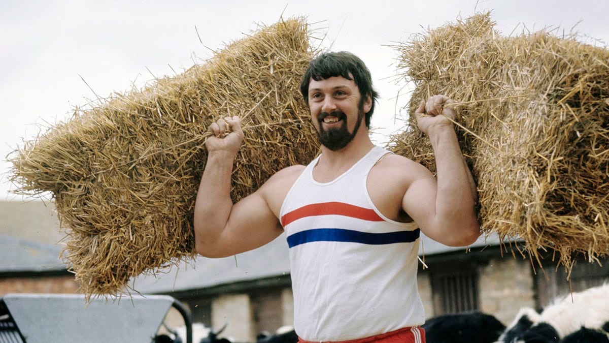 Geoff Capes holds straw bales