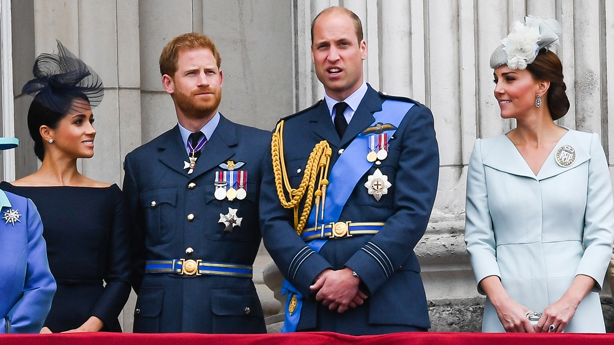 The royal family looks serious and stands on the balcony of the palace.