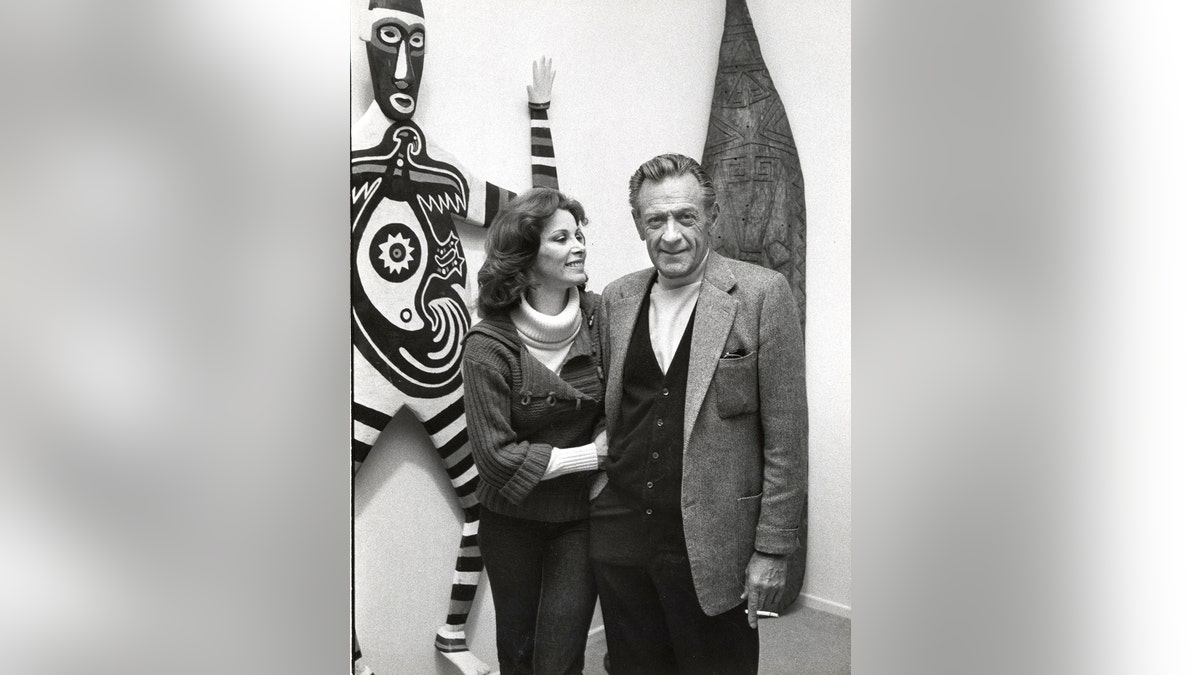 Stefanie Power on the arm of William Holden in front of African art.