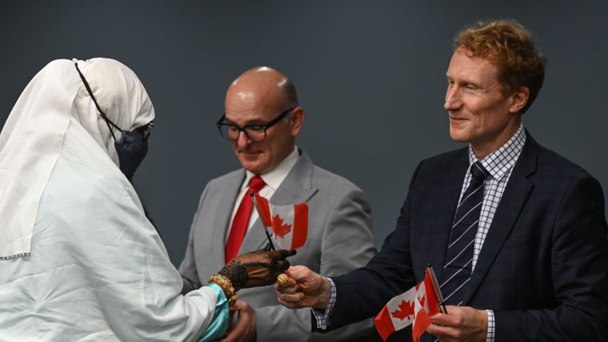 Marc Miller (R), Ministro de Inmigración, Refugiados y Ciudadanía, entrega una pequeña bandera canadiense a uno de los 53 nuevos ciudadanos canadienses que representan a 22 naciones diversas, mientras se embarcan en su viaje hacia la ciudadanía durante una ceremonia especial en Canada Place, el 12 de octubre de 2023. , en Edmonton, Alberta, Canadá.