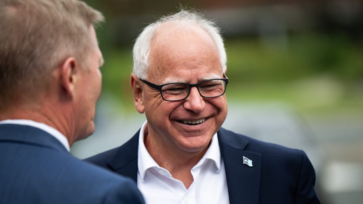 Tim Walz, homem de cabelos brancos, sorrindo com óculos de aros pretos