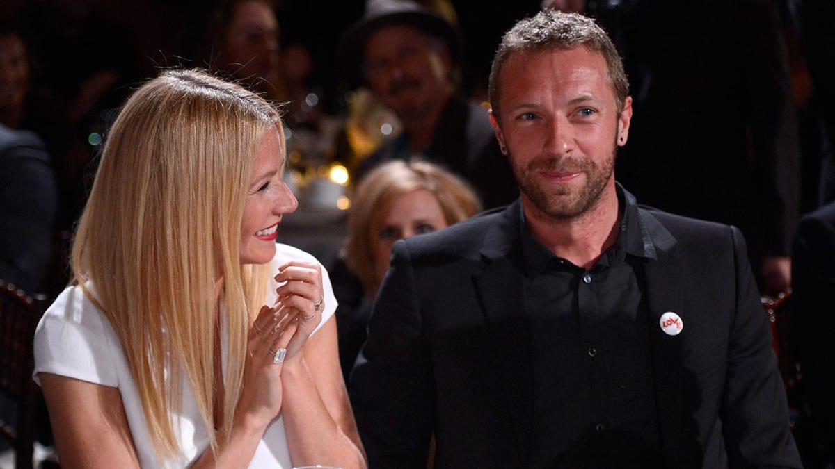 Gwyneth Paltrow successful  a achromatic  formal  grins and claps for hubby  Chris Martin successful  a achromatic  suit   sitting astatine  a table