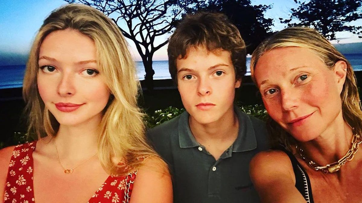 Apple Martin in a red patterned dress takes a selfie with brother Moses in a collared shirt and mother Gwyneth Paltrow