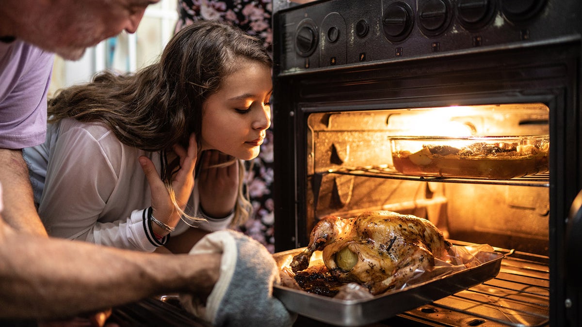 Grandfather and young miss  taking a cooked turkey retired  of the oven.