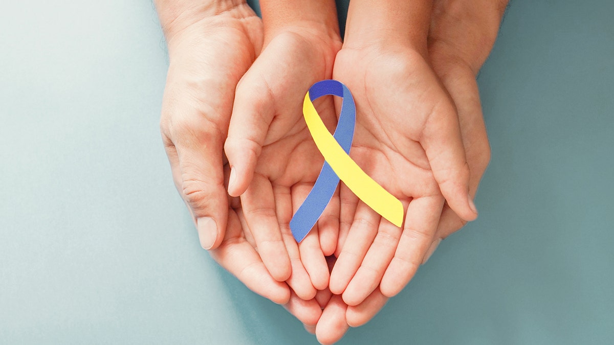 Adult and kid  hands holding bluish  and yellowish  ribbon for Down syndrome awareness