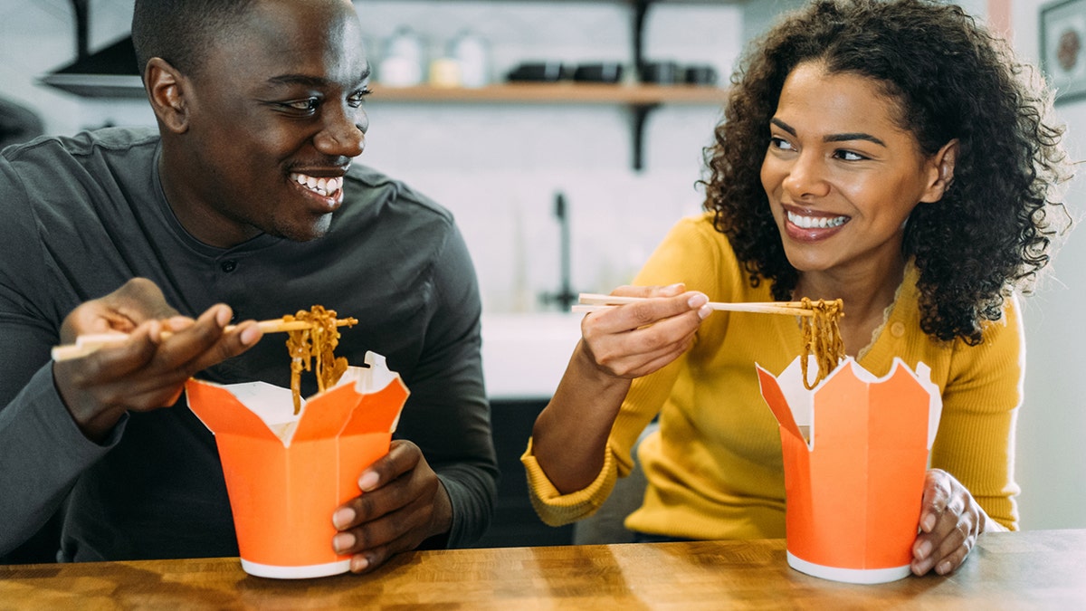 Hombre y mujer comiendo comida china para llevar en cajas de cartón en casa.