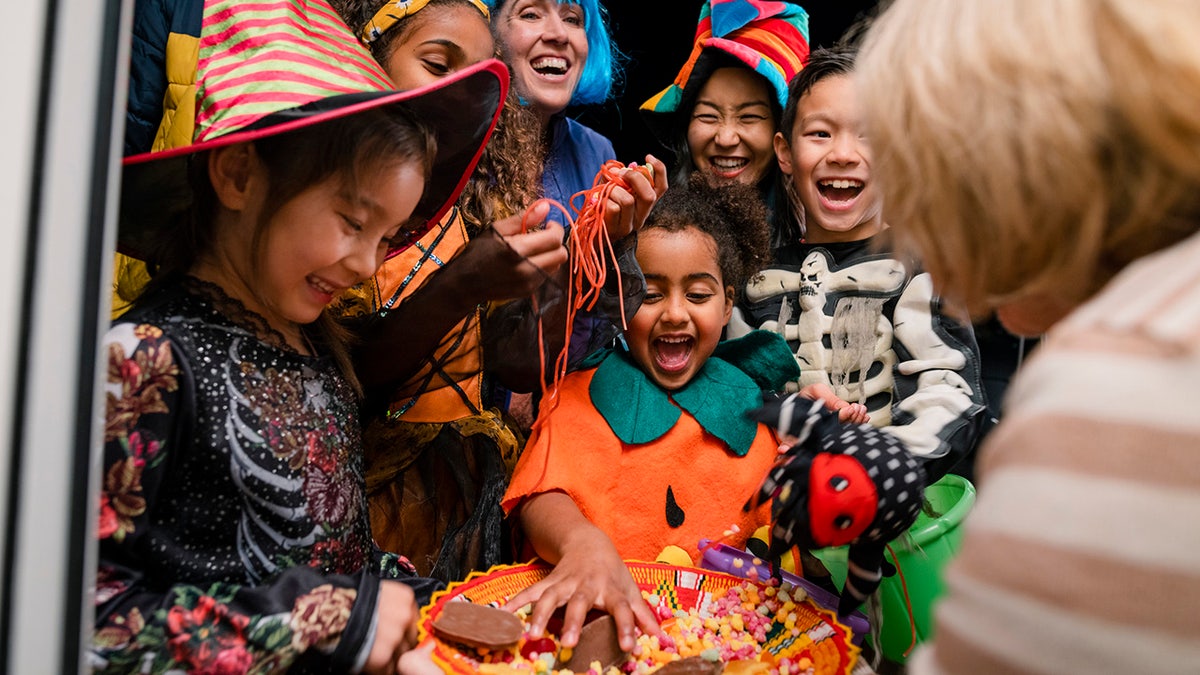 Children in costumes taking candy from a bowl.