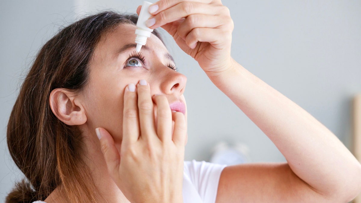 Young woman putting eye drops at home