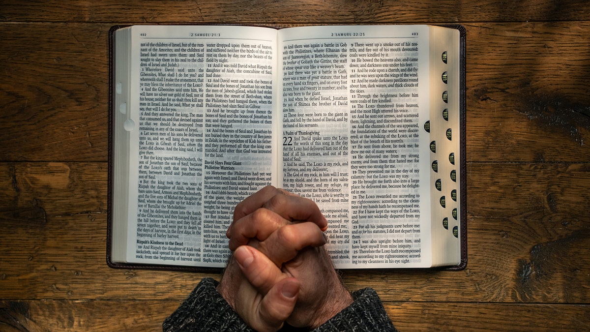 People clutch with their hands in prayer on the open sides of a Bible.