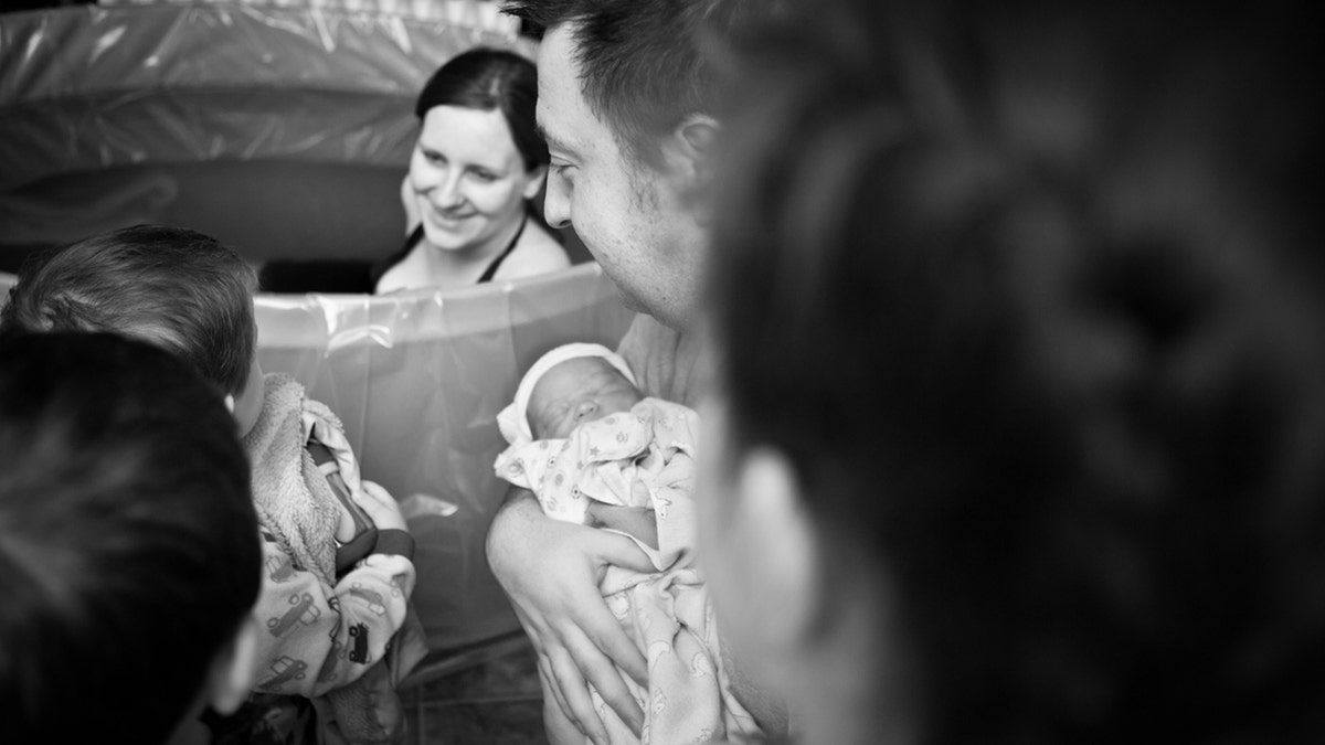 father showing his newborn lad   to his different   children arsenic  their parent  looks on