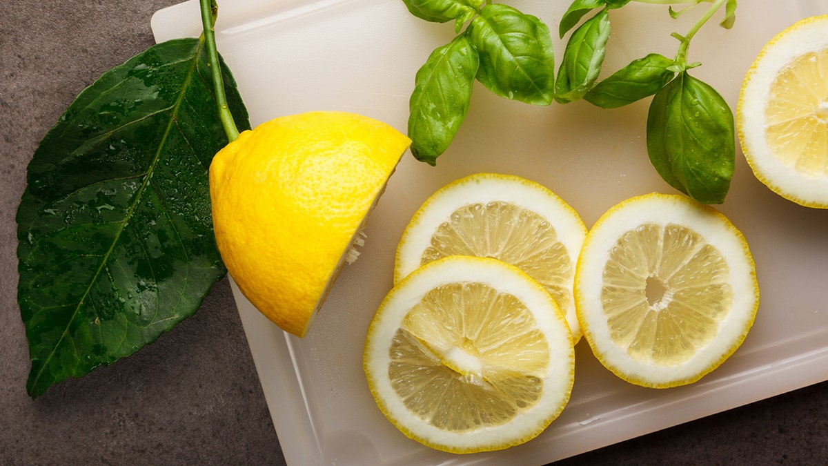 Fresh sliced lemons and basil connected  a cutting board.