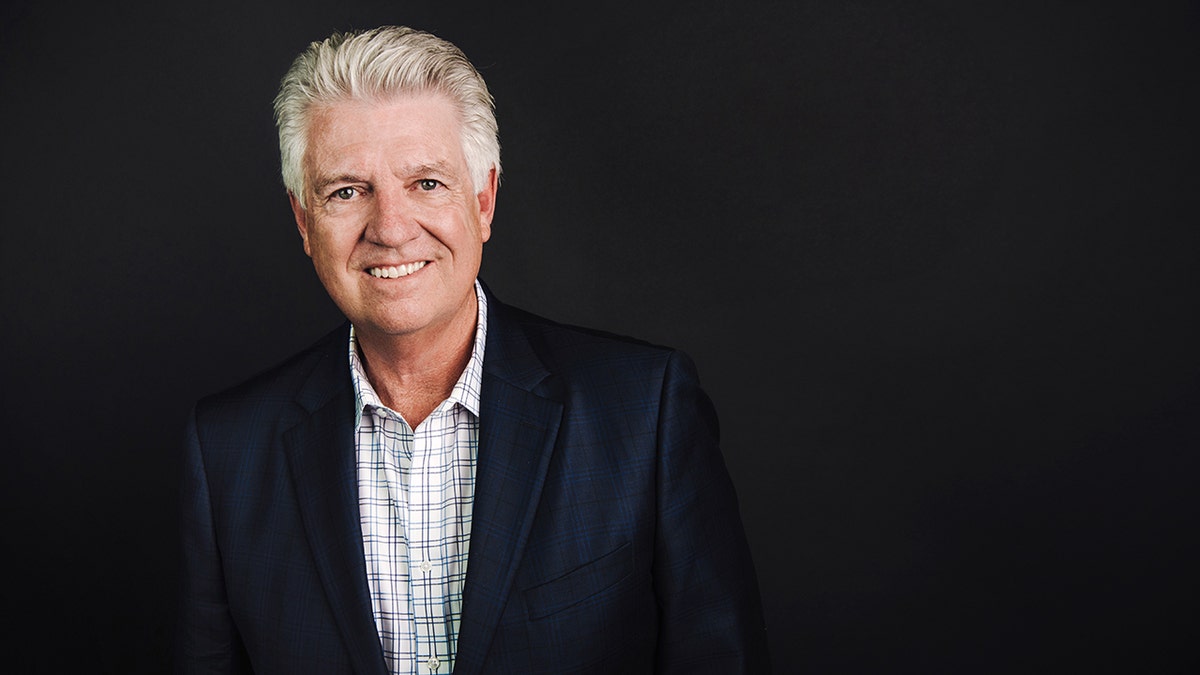 Foto Dr. Jack Graham, seorang pria kulit putih dengan rambut beruban, mengenakan kemeja kotak-kotak di bawah blazer biru. Dia tersenyum. 