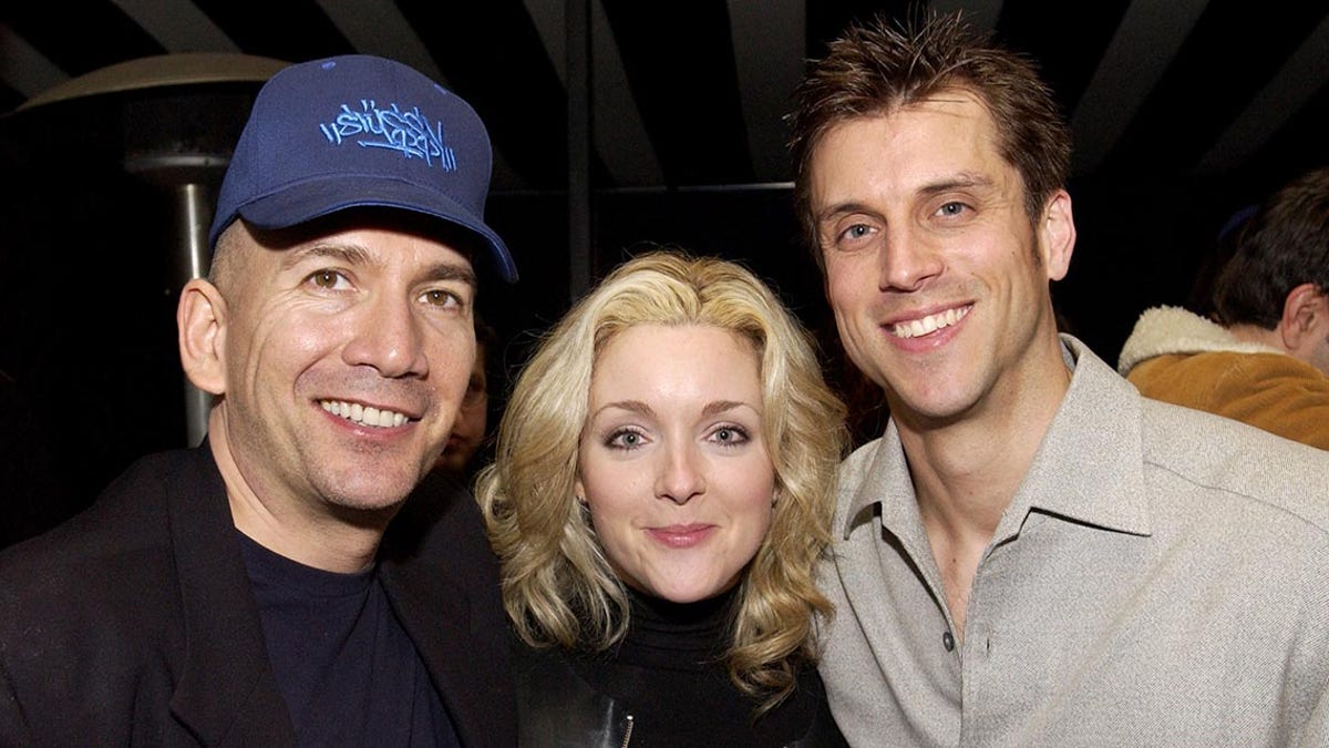 Jack Merill in a black suit smiles next to Jane Krakowski and another man in a light gray shirt