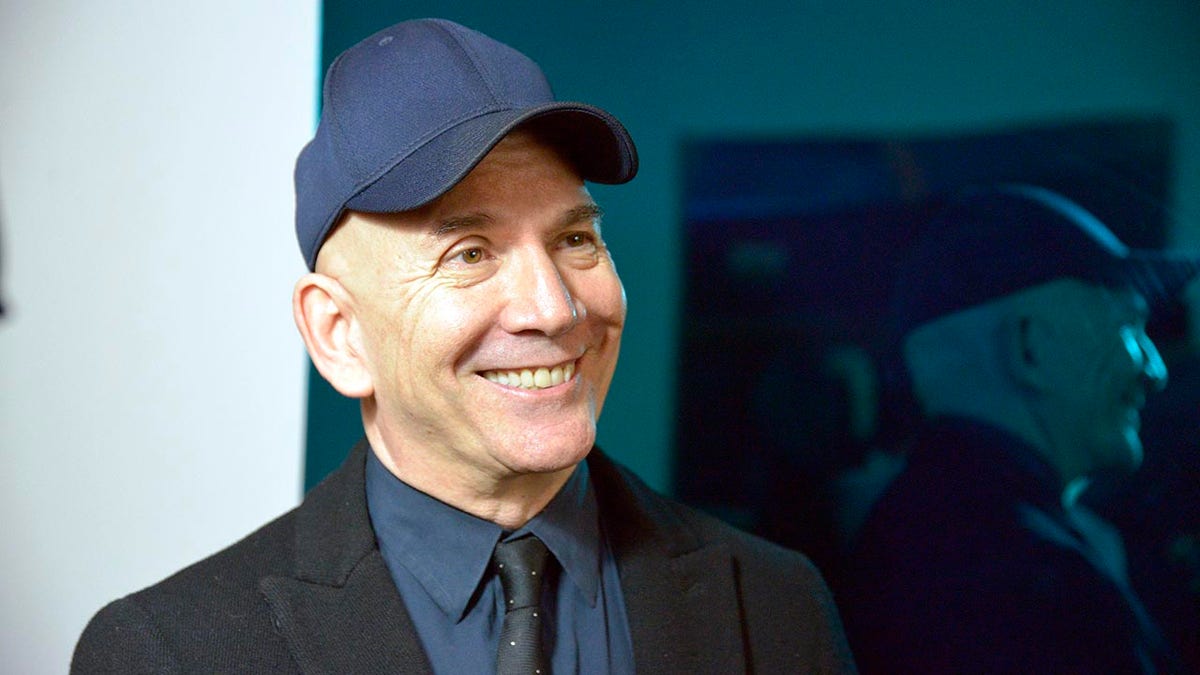 Actor Jack Merrill successful  a bluish  shot   headdress  smiles wearing a achromatic  suit   overgarment   and navy bluish  shirt, representation   taken from angle