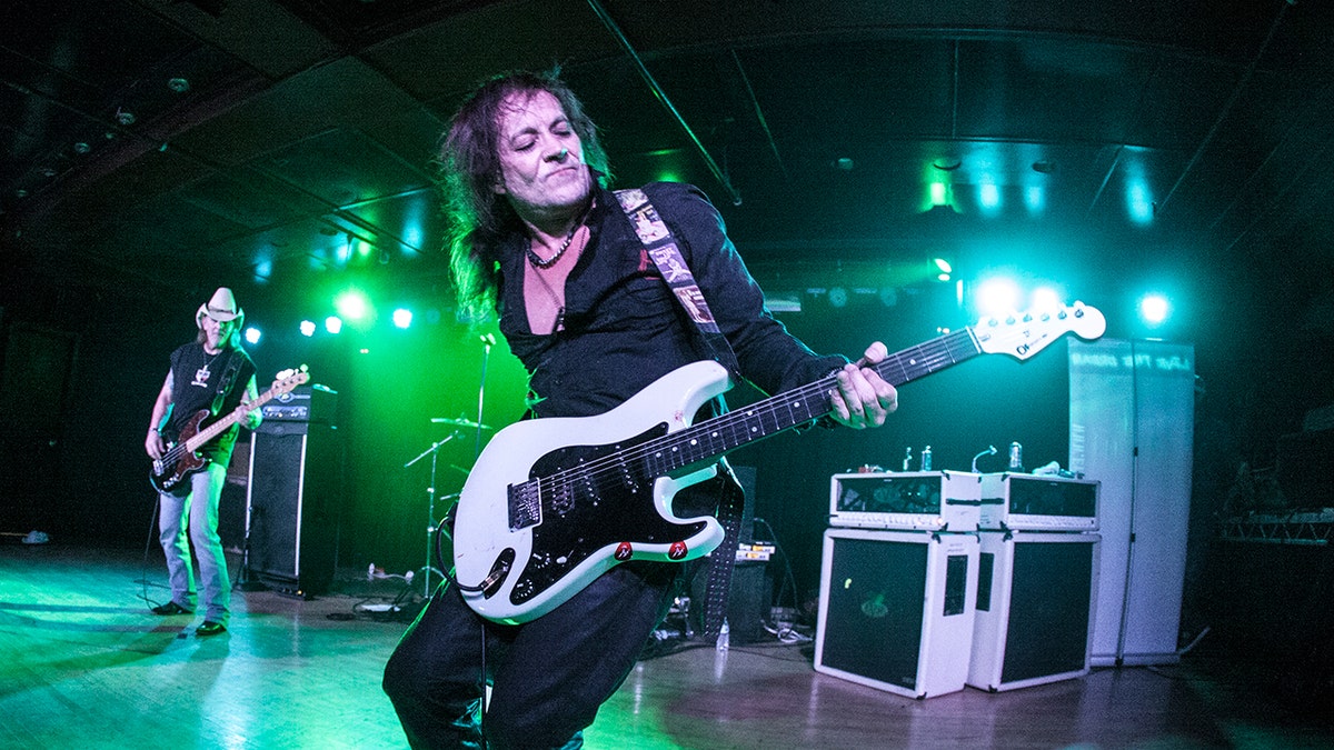 Jake E. Lee toca guitarra no palco durante um show.