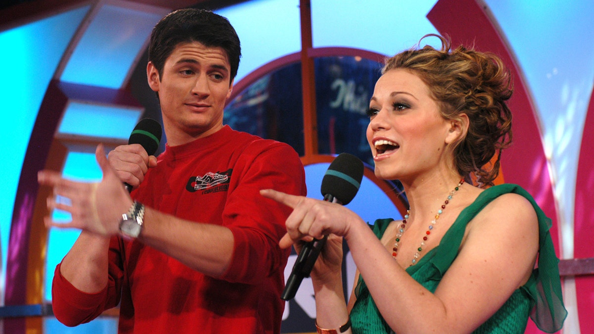 James Lafferty in a red shirt with a microphone looks down on Bethany Joy Lenz in a green shirt with a microphone